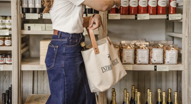 Guest carrying an Estancia Vigil market tote past shelves of preserves and wine