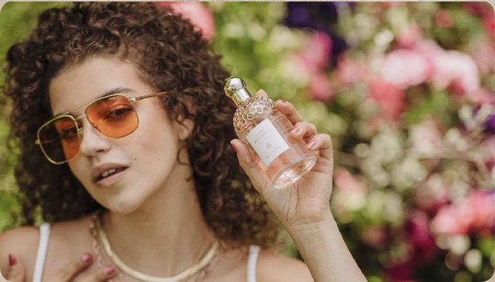Guest in sunglasses holding the Aqua Allegoria bottle among garden flowers