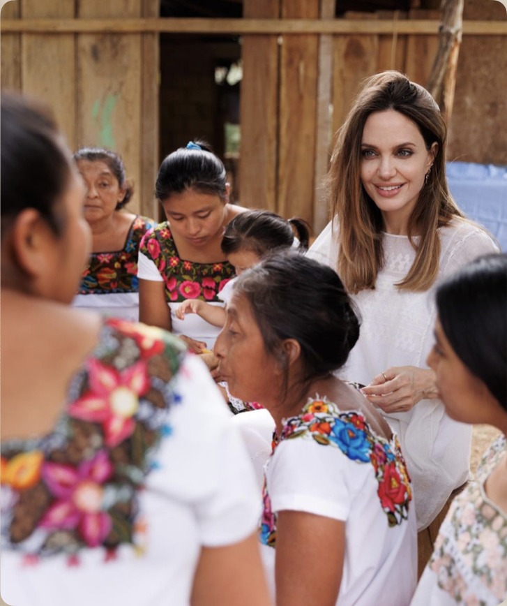 Close-up of Angelina Jolie in conversation with Mayan artisan women wearing embroidered huipils