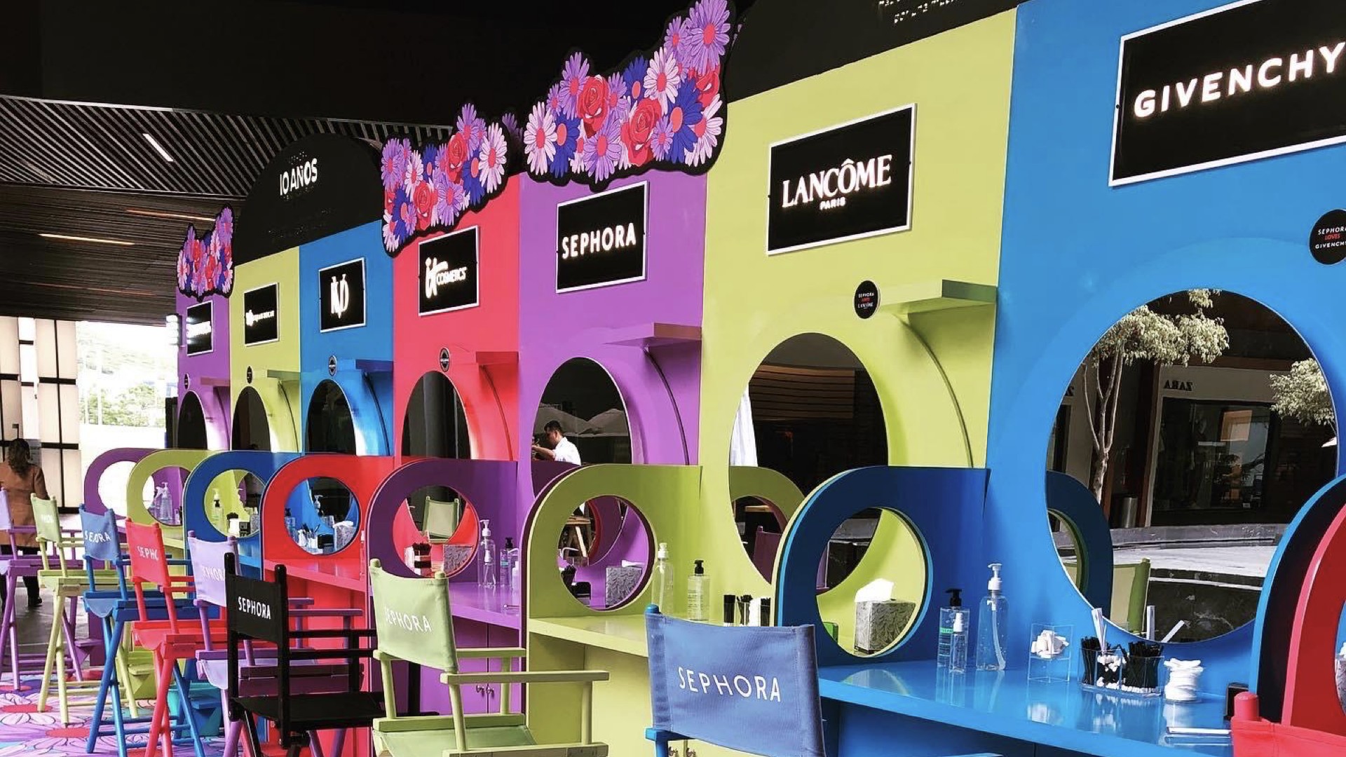 Row of colorful anniversary kiosks for Sephora, Sephora Collection, Lancôme, and Givenchy, each with a round cutout mirror and matching director's chairs
